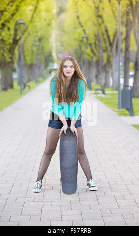 Portrait of beautiful teenage girl with skateboard in green park Stock Photo