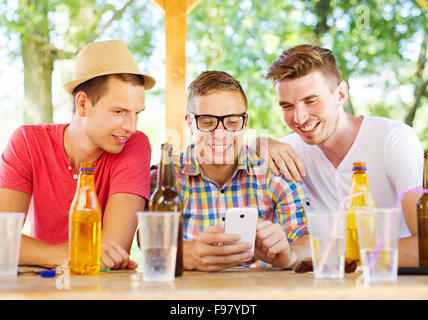 Three happy friends drinking and having fun with smartphone in pub garden Stock Photo