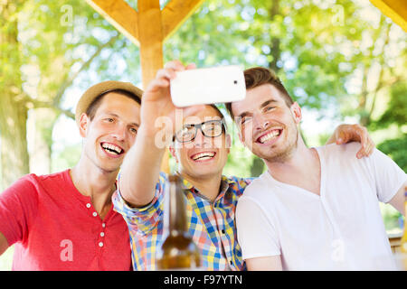 Three happy friends drinking and taking selfie with smartphone in pub garden Stock Photo