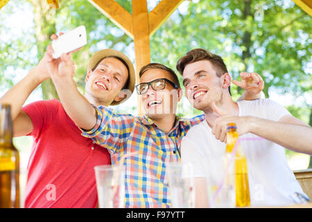 Three happy friends drinking and taking selfie with smartphone in pub garden Stock Photo