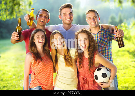 Group of happy friends spending free time together in park and drinking beer Stock Photo