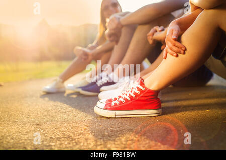 Legs and sneakers of teenage boys and girls sitting on the sidewalk Stock Photo