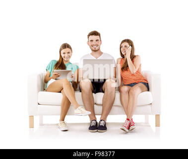 Three young people sitting on sofa and using wireless technologies, isolated on white background. Best friends Stock Photo