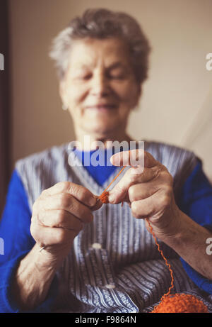 Portrait of senior woman sitting in armchair and knitting at home Stock Photo