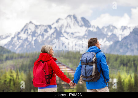 Senior hikers couple during the walk in beautiful mountains, hills and hotel in background Stock Photo