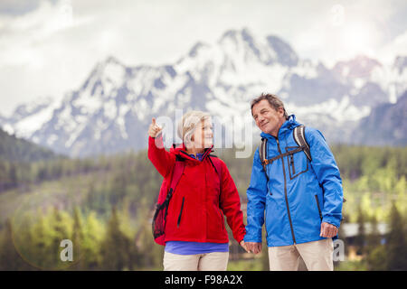 Senior hikers couple during the walk in beautiful mountains, hills and hotel in background Stock Photo