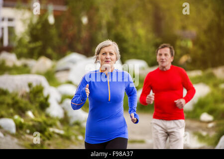 Senior couple jogging round the tarn in beautiful mountains, hills and hotel in background Stock Photo