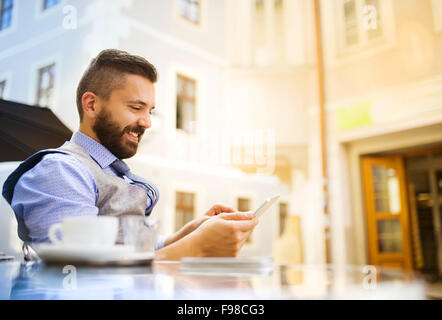 Modern hipster businessman drinking espresso coffee in the city cafe during lunch time and using mobile phone Stock Photo