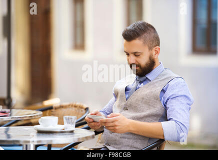 Modern hipster businessman drinking espresso coffee in the city cafe during lunch time and using mobile phone Stock Photo