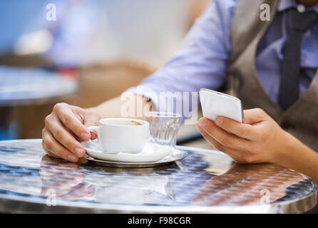 Detail of businessman drinking espresso coffee in the city cafe during lunch time and using mobile phone Stock Photo
