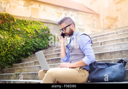 Handsome hipster modern businessman using smart phone and laptop in the city Stock Photo