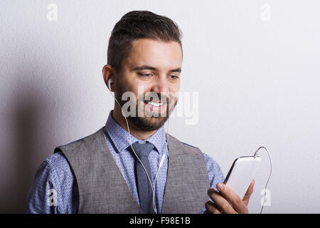 Studio shot of modern hipster businessman with headphones, listening to music from mobile phone Stock Photo