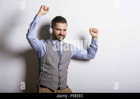 Studio shot of modern hipster businessman with headphones, listening to music and dancing Stock Photo
