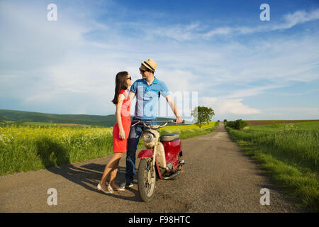 Happy young couple in love with retro motorbike is kissing on road near the field Stock Photo