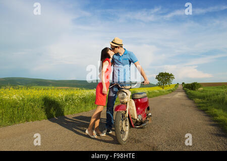 Happy young couple in love with retro motorbike is kissing on road near the field Stock Photo