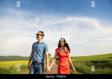 Happy young couple in love walking and holding hands on countryside road next to the colza field Stock Photo