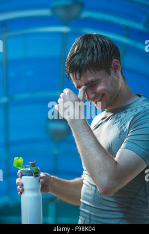Man fitness runner drinking and splashing water in his face. Funny image of handsome male refreshing during workout Stock Photo