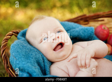 Happy baby boy lying in the basket with apples in nature Stock Photo