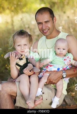 Happy young father spending time with his little daughters in green nature. Stock Photo