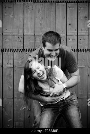 Black and white portrait of happy young couplehaving fun in front of fence in garden Stock Photo