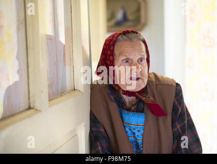 Very old woman is standing by the door and looking to the camera at her country style house Stock Photo