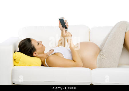 Studio portrait of pregnant woman with digital tablet lying down on sofa isolated on white background Stock Photo