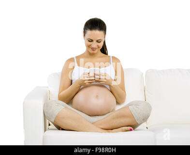 Studio portrait of pregnant woman with smartphone sitting on sofa isolated on white background Stock Photo