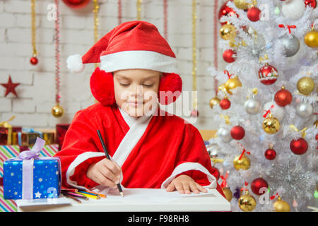 Six year old girl dressed in a red suit Santa Claus draws pencils are in a festive Christmas interior Stock Photo