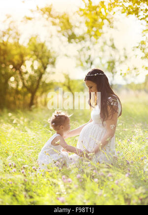 Cute little girl touching her mother's pregnant belly in summer nature Stock Photo