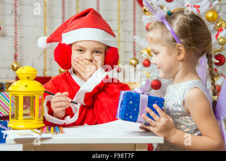 A girl dressed in a red suit Santa Claus draws pencils sitting at the table, next is a girl dressed as a fairy with the candlest Stock Photo