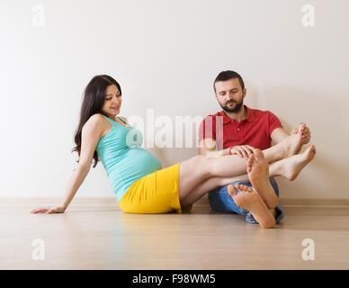 Young couple is sitting on the floor in their empty new house. Woman is pregnant. Stock Photo