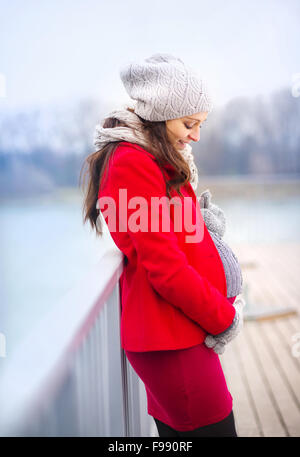 Pregnant woman in knitted clothes holding her belly, outside in winter weather Stock Photo