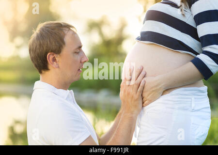 Man is kissing pregnant woman's belly in nature Stock Photo