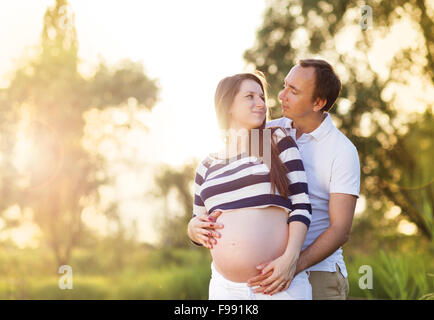 Happy young pregnant couple hugging in nature Stock Photo