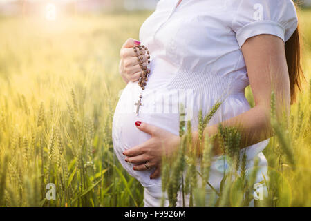 Outdoor portrait of unrecognizable young pregnant woman praying in the field Stock Photo