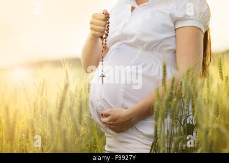 Outdoor portrait of unrecognizable young pregnant woman praying in the field Stock Photo