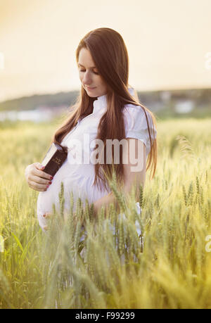 Outdoor portrait of young pregnant woman praying in the field Stock Photo