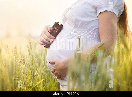 Outdoor portrait of unrecognizable young pregnant woman praying in the field Stock Photo