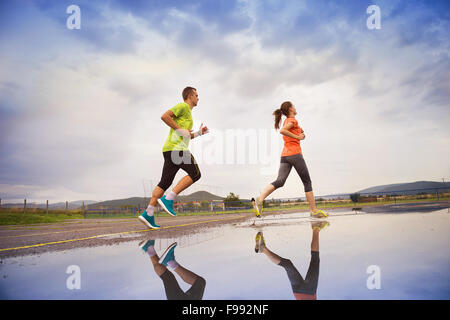 Young couple running on asphalt in rainy weather splashing in puddles. Stock Photo