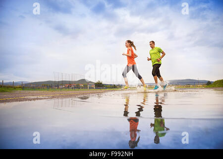 Young couple running on asphalt in rainy weather splashing in puddles. Stock Photo