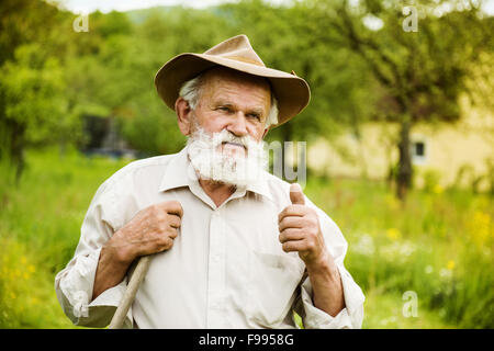 Old farmer with beard working with rake in garden Stock Photo