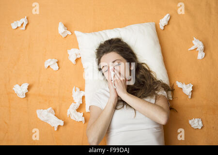 Sick woman lying in bed with cold and flu. She is blowing nose.