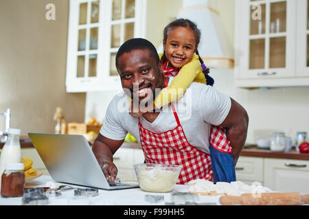 Young man looking for recipe in the net with daughter on his back Stock Photo
