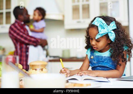 Cute schoolgirl making notes in exercise-book at home Stock Photo