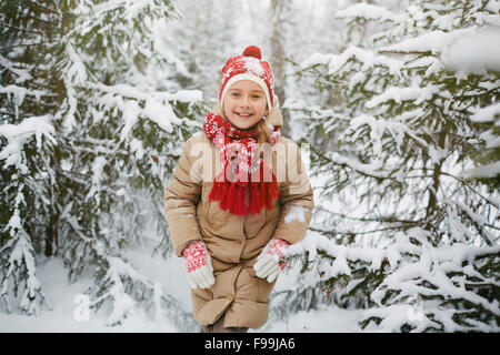 Happy little girl in winter park standing among fir-trees Stock Photo