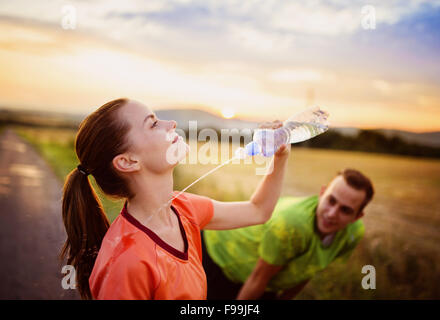 Cross-country trail running couple having water break at sunset Stock Photo