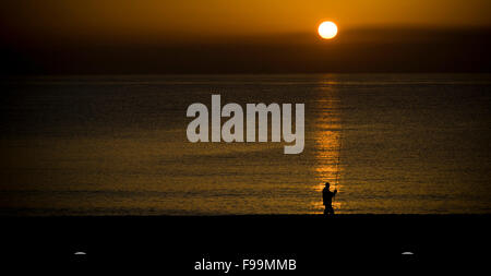 A fisherman casts his fishing rod to Mediterranean sea as the sun rises in Barcelona coast. Stock Photo