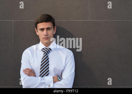 Portrait of serious and confident adult businessman wearing shirt and necktie with arms crossed in front of gray wall with copys Stock Photo