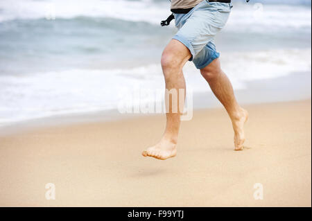 Detail of male feet running at the sandy beach Stock Photo