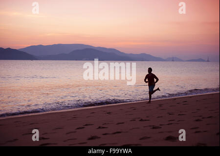 Young man running on the beach at sunset Stock Photo